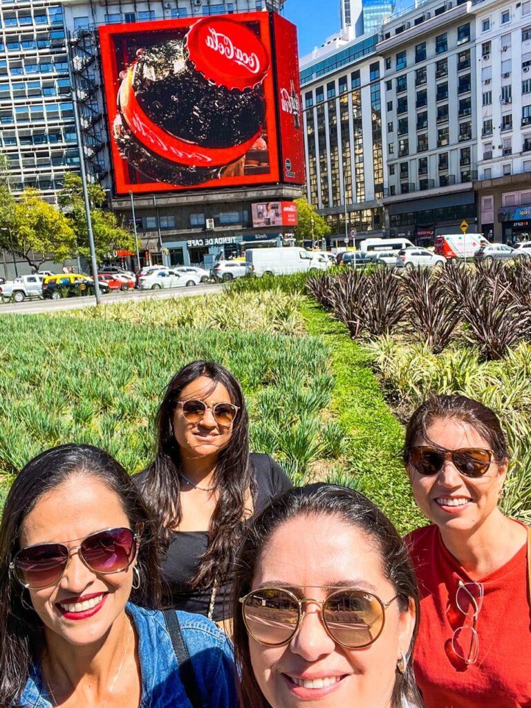 Grupo de turistas em Buenos Aires próximo ao Obelisco, com painel 3D ao fundo.